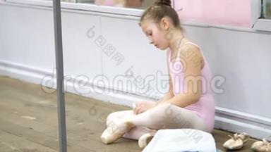 十几岁的小女孩穿着粉红色紧身衣，在芭蕾舞学校准备古典芭蕾舞蹈课。 她穿上了